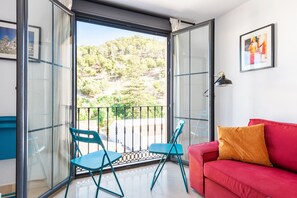Un balcone con un divano rosso e due poltrone, una porta in vetro e vista sul verde.