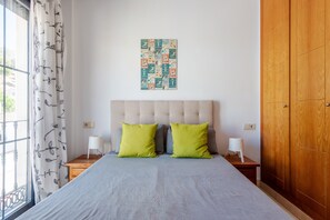 A bedroom with a bed, two nightstands, a wooden wardrobe, a window with curtains, and a wall art piece. - Apartment 'El Ático De La Montaña' with Balcony, Wi-Fi and Air Conditioning (Málaga)