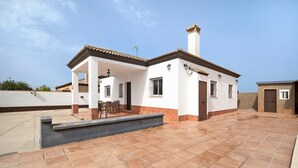 Ein zweistöckiges Haus mit Terrasse, überdachter Sitzgruppe und Schornstein.