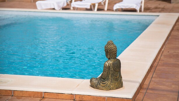 Ein Pool mit einer Buddha-Statue, weißen Liegestühlen und einer gefliesten Liegefläche.