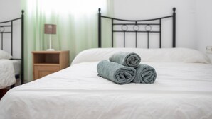 Ein ordentlich gemachtes Bett mit aufgerollten Handtüchern, ein Nachttisch mit Lampe und ein grüner Vorhang in einem Hotelzimmer.