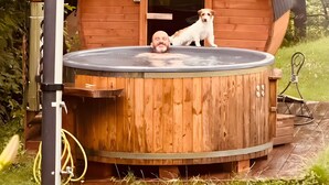 A wooden hot tub with a dog inside, surrounded by greenery. - Holiday Home 'La Rosa sul Lago' Pet-Friendly with Private Garden, Spa, and Wi-Fi (Osiglia)