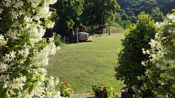 A wooden pergola with white flowers, a grassy lawn, and a view of a forested hill. - Holiday Home 'La Rosa sul Lago' Pet-Friendly with Private Garden, Spa, and Wi-Fi (Osiglia)