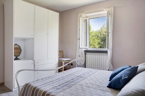 A bedroom with a bed, a window with curtains, a radiator, and a wardrobe.