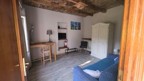 Une pièce comprenant un bureau en bois, une chaise, un canapé bleu, une armoire blanche et un téléviseur fixé au mur.