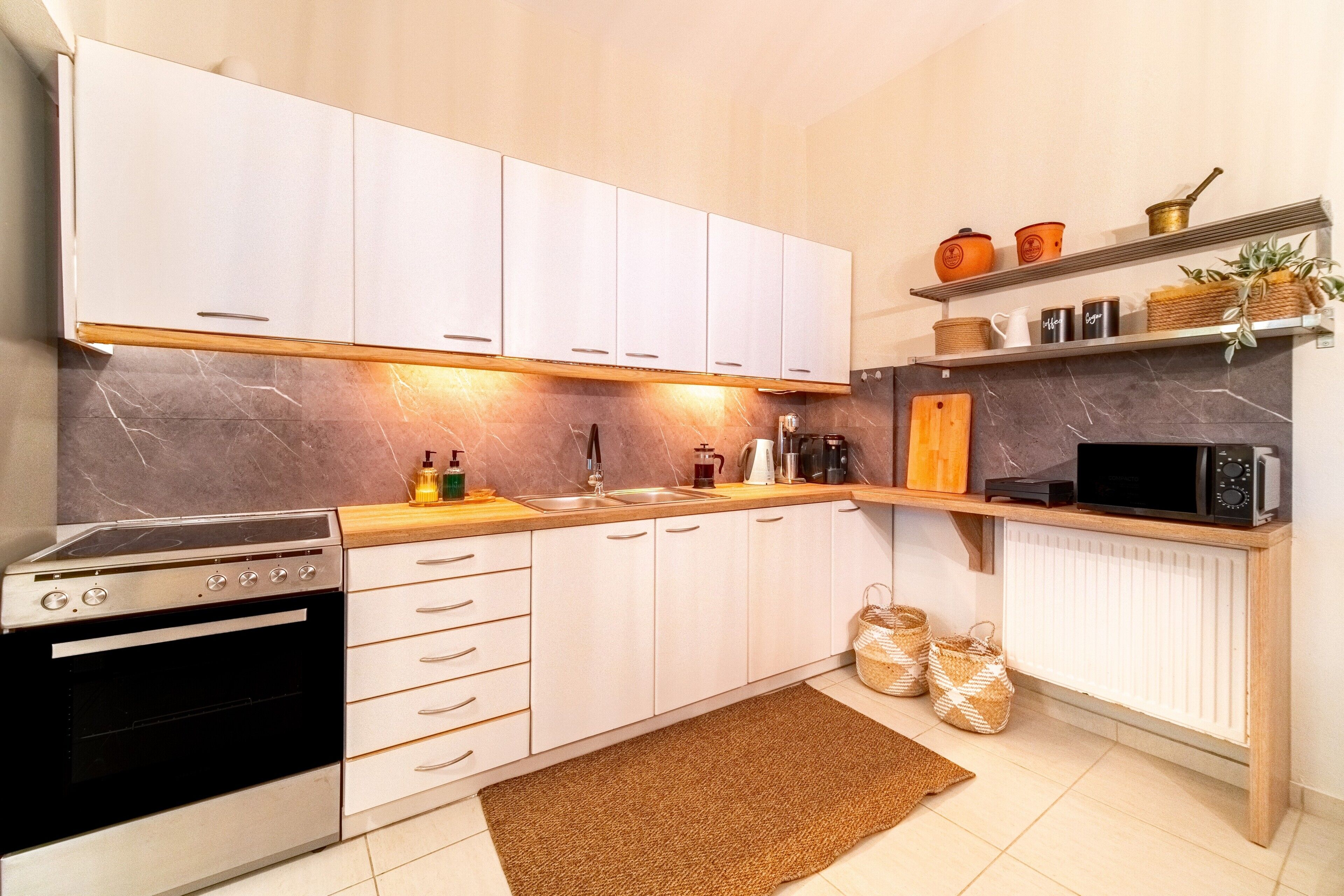 A modern kitchen with white cabinets, a microwave, a coffee maker, and a stove.