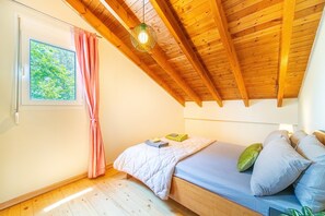 A bedroom with a wooden ceiling, a bed with pillows, a window with curtains, and a hanging light fixture.