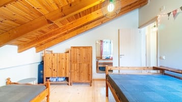 Una habitación con techo inclinado, vigas de madera, literas, un armario y un espejo.