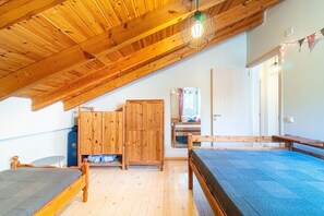 A room with a sloped ceiling, wooden beams, bunk beds, a wardrobe, and a mirror.