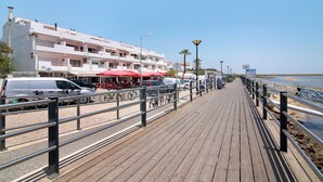 A wooden boardwalk leading to a beach with a white building and red umbrellas.