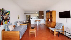 A living room with a sofa, a wooden table, a TV, and a kitchen in the background.