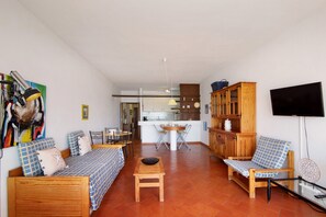 A living room with a sofa, a wooden table, a TV, and a kitchen in the background.