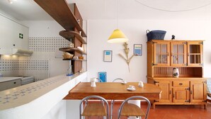 A kitchen with a wooden table, chairs, a hanging lamp, and a cabinet with glass doors.