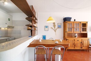A kitchen with a wooden table, chairs, a hanging lamp, and a cabinet with glass doors.
