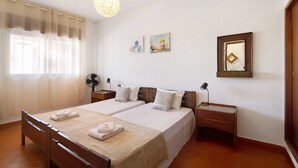 A double bed with a wooden headboard, two bedside tables with lamps, a wall-mounted mirror, and a ceiling fan.