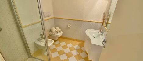 A bathroom with a glass shower enclosure, a toilet, a sink, and a checkered floor.