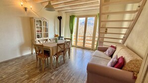 Um quarto acolhedor com uma mesa de jantar de madeira, cadeiras, um sofá e uma janela grande com vista para o exterior.