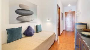 Un dormitorio con cama, almohadas, un cuadro, una puerta de madera y suelo de baldosas.