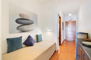 A bedroom with a bed, pillows, a painting, a wooden door, and a tiled floor.
