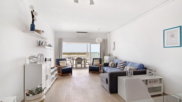 Una sala de estar moderna con un sofá, sillas, una mesa de centro de cristal, un armario blanco y vistas al exterior.