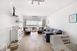Un salon moderne avec un canapé, des fauteuils, une table basse en verre, un meuble blanc et une vue sur l’extérieur.