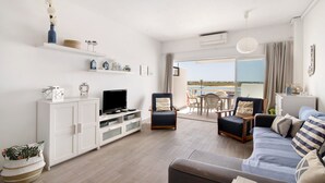 Una sala de estar moderna con un sofá, sillones, televisor y un balcón con vistas.
