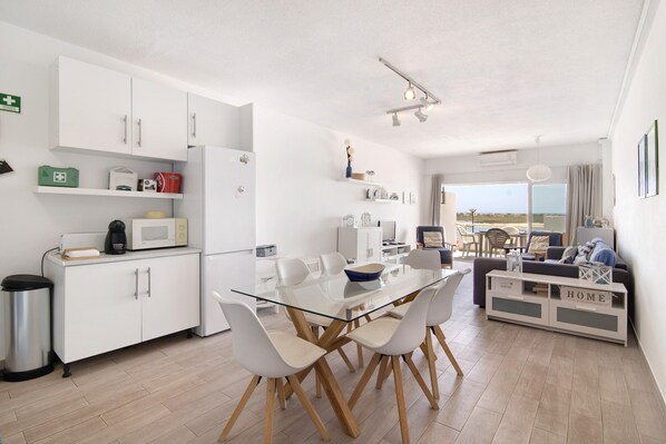 Une cuisine moderne avec des meubles blancs, une table à manger en verre et une vue sur l’extérieur.