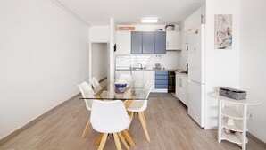 Una cocina moderna con armarios blancos, una mesa de comedor de vidrio y una pequeña mesita auxiliar blanca.