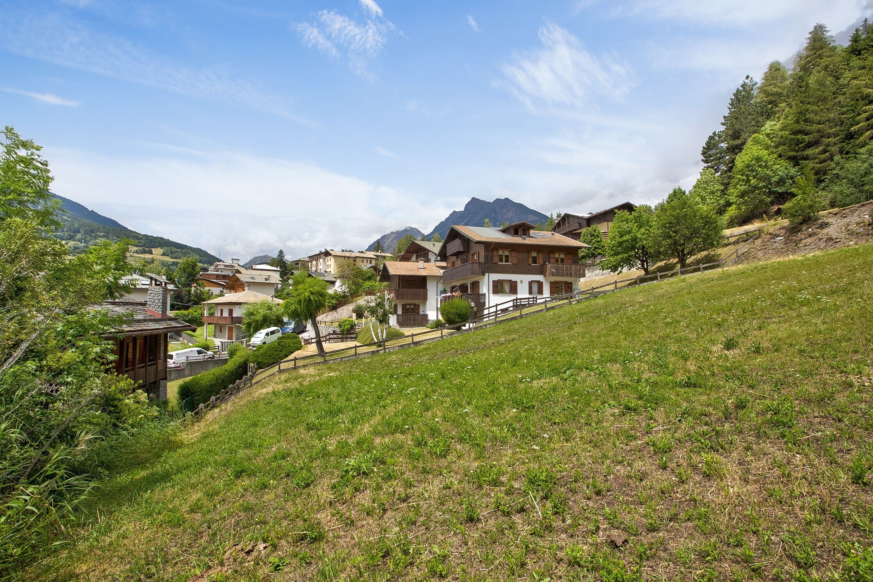 A hillside village with traditional houses, a wooden fence, and a mountain backdrop.