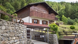 A chalet with a stone wall entrance, wooden balcony, and a view of a forested hillside. - Apartment 'Chalet Holly' with Mountain View, Shared Garden and Wi-Fi (Bormio)