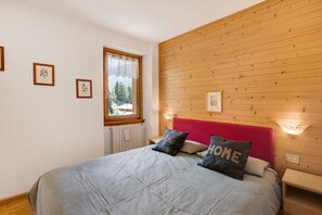 A bedroom with a wooden headboard, a bed with a grey quilt, and a window with a view of trees.