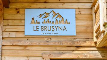 A wooden sign with a mountain and tree design, labeled 'LE BRUSYNA LOCATION CHALET.'