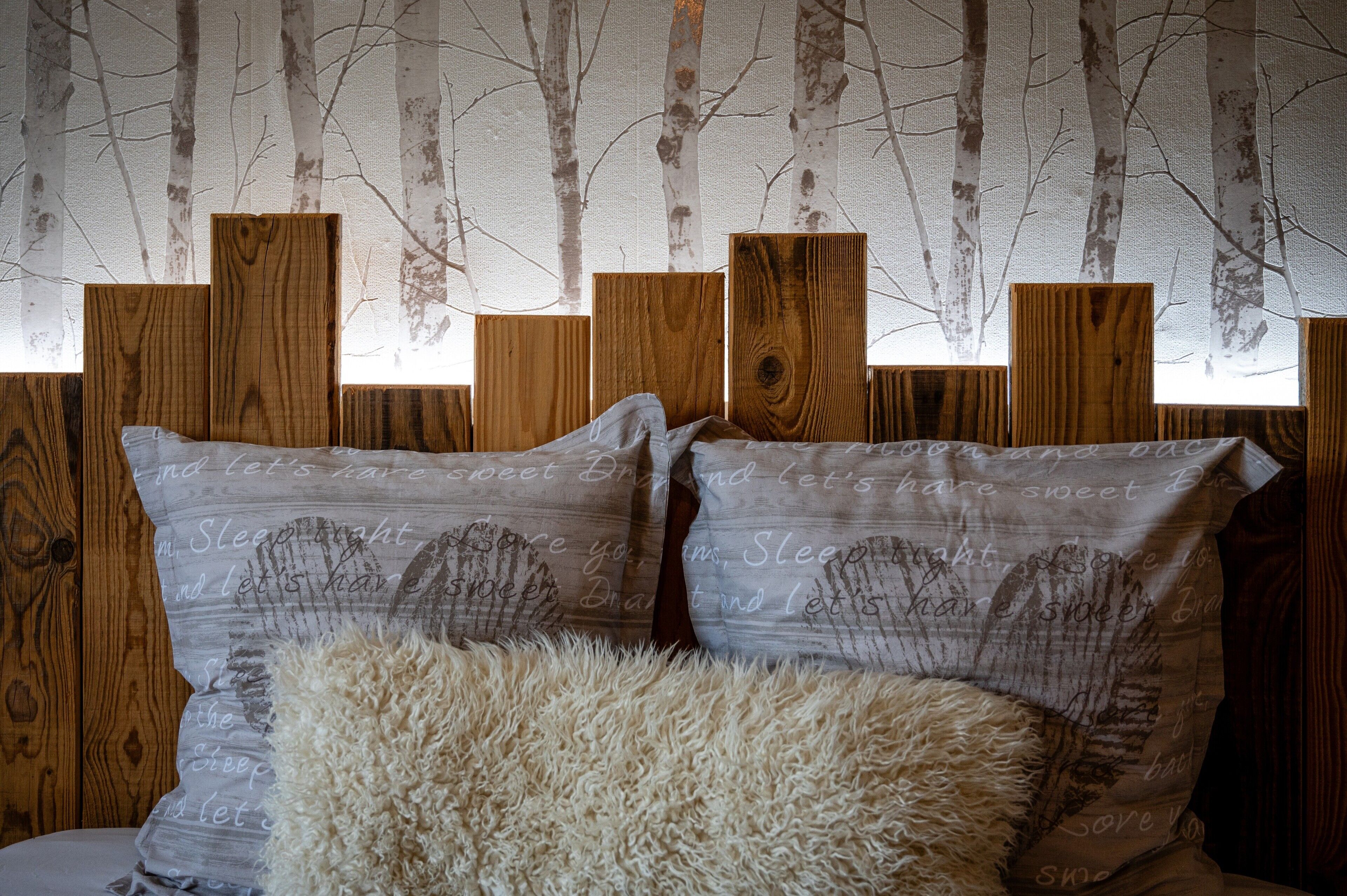 Un dormitorio con cabecera de madera, dos almohadas con texto y un edredón mullido.