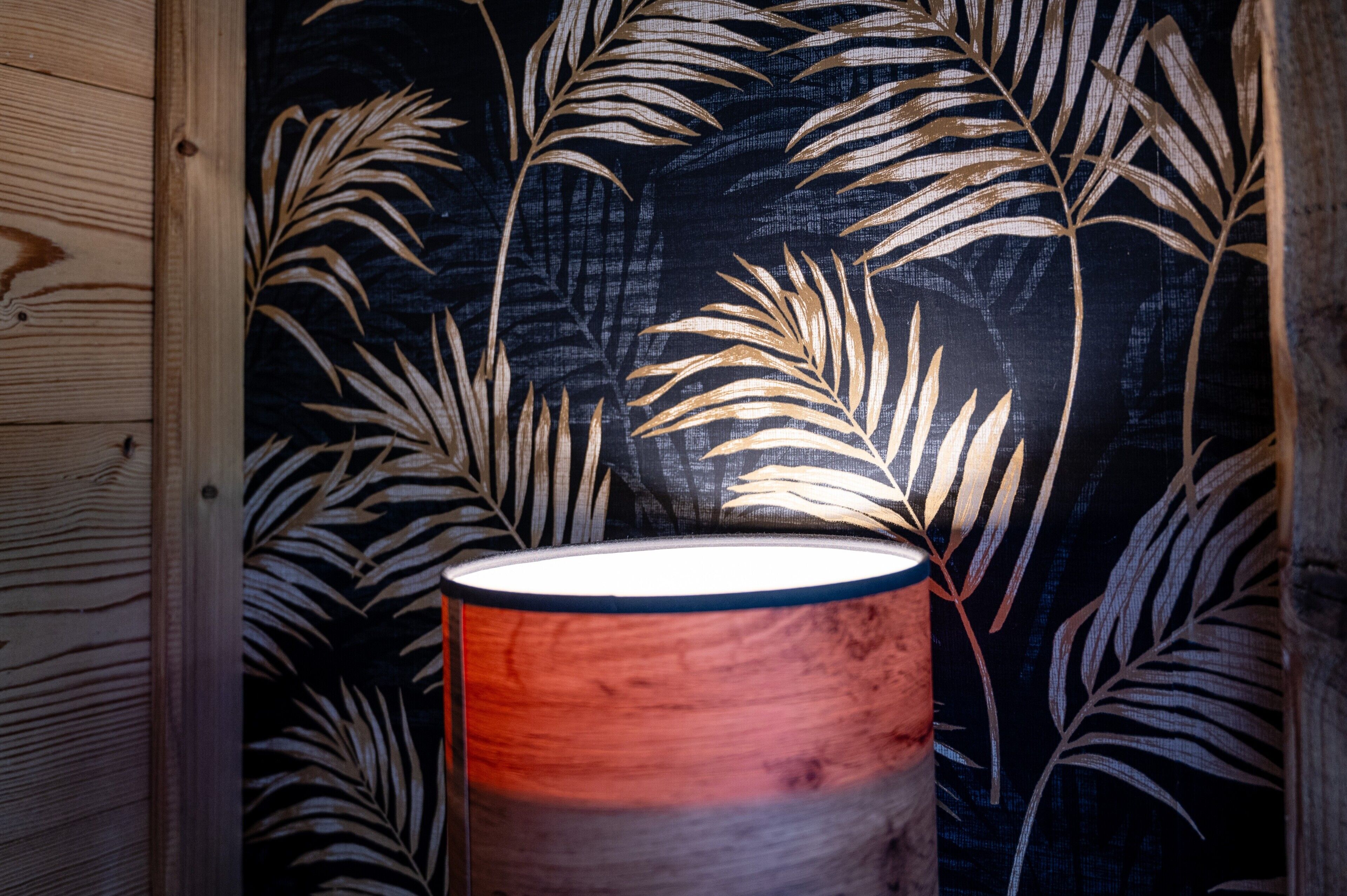 A lamp with a gradient shade in front of a wall with a leaf pattern.