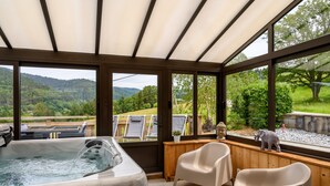 Wellnessbereich mit Whirlpool, Holzterrasse und Stühlen mit Blick auf eine Berglandschaft.