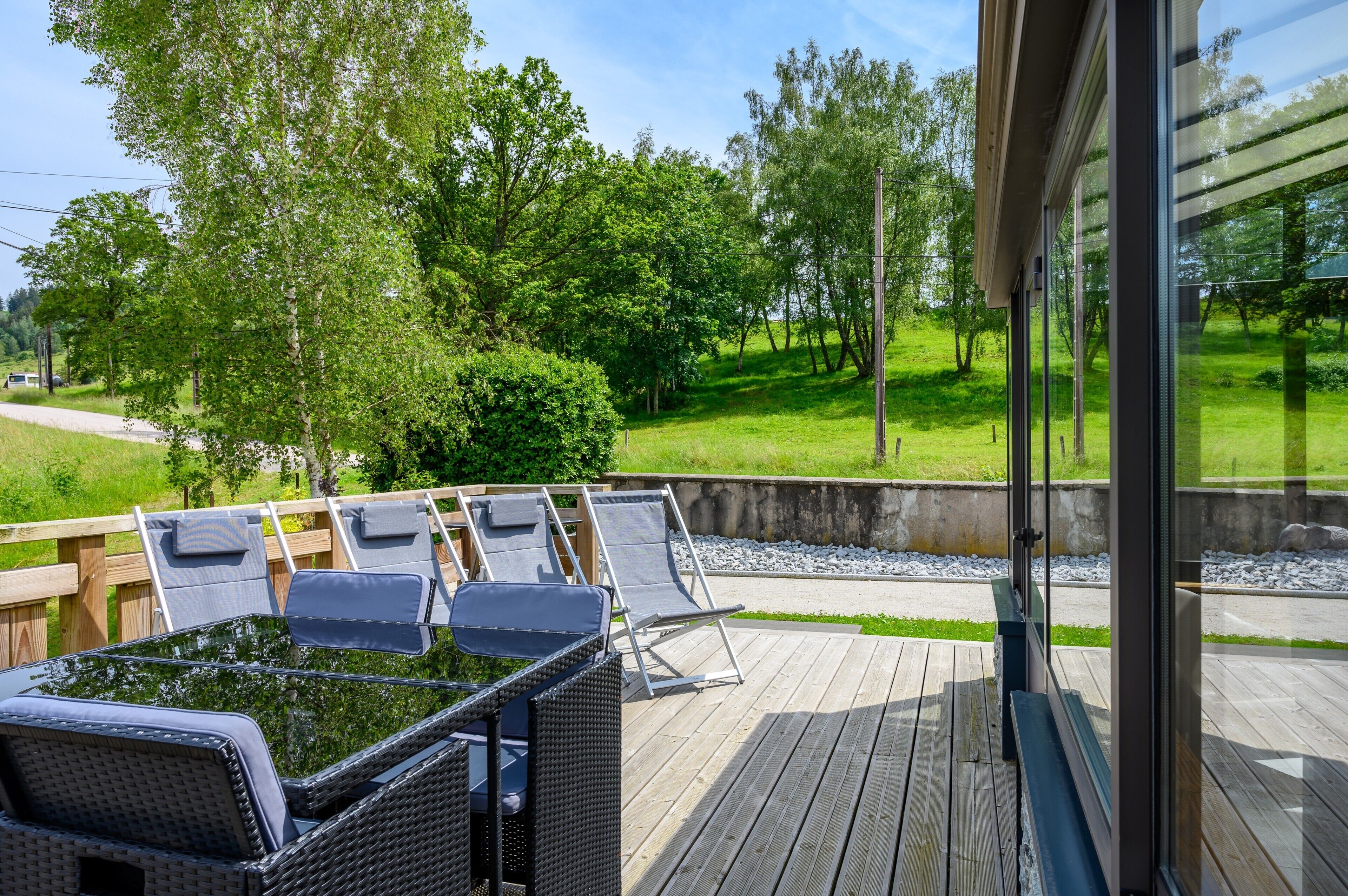 Eine Terrasse mit Gartenmöbeln, Blick auf eine Rasenfläche und ein Holzzaun.