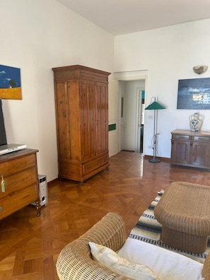 A living room with a wooden cabinet, a television on a wooden dresser, a wicker sofa, and a patterned rug.