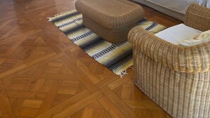 Ein Wohnzimmer mit einer Couch, einem Hocker und Korbmöbeln, einem Bild an der Wand und einer Tür, die nach draußen führt.
