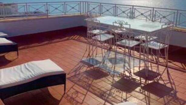 Eine Dachterrasse mit Liegestühlen und einem Tisch, mit Blick auf das Meer.