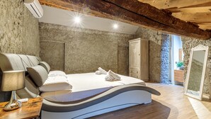Een slaapkamer met een gebogen bed, een massagestoel, een houten nachtkastje en een stenen muur.