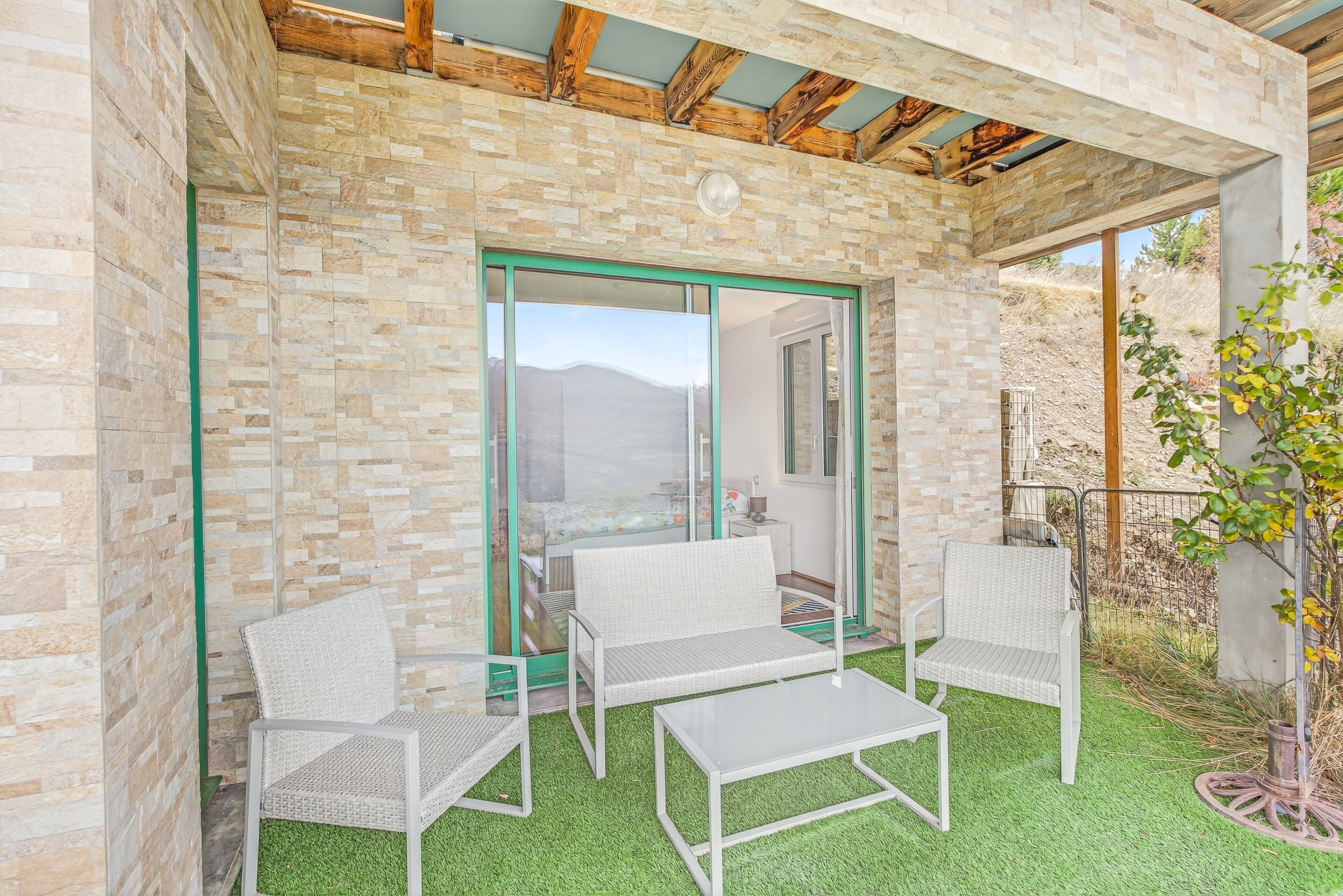 Un patio con due sedie in vimini e un tavolo, un muro in pietra e vista su un paesaggio montuoso.
