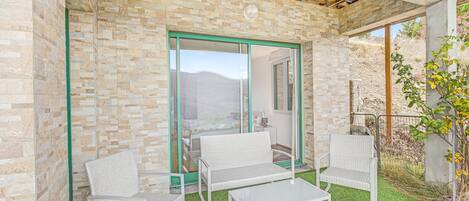 Un patio con due sedie in vimini e un tavolo, un muro in pietra e vista su un paesaggio montuoso.