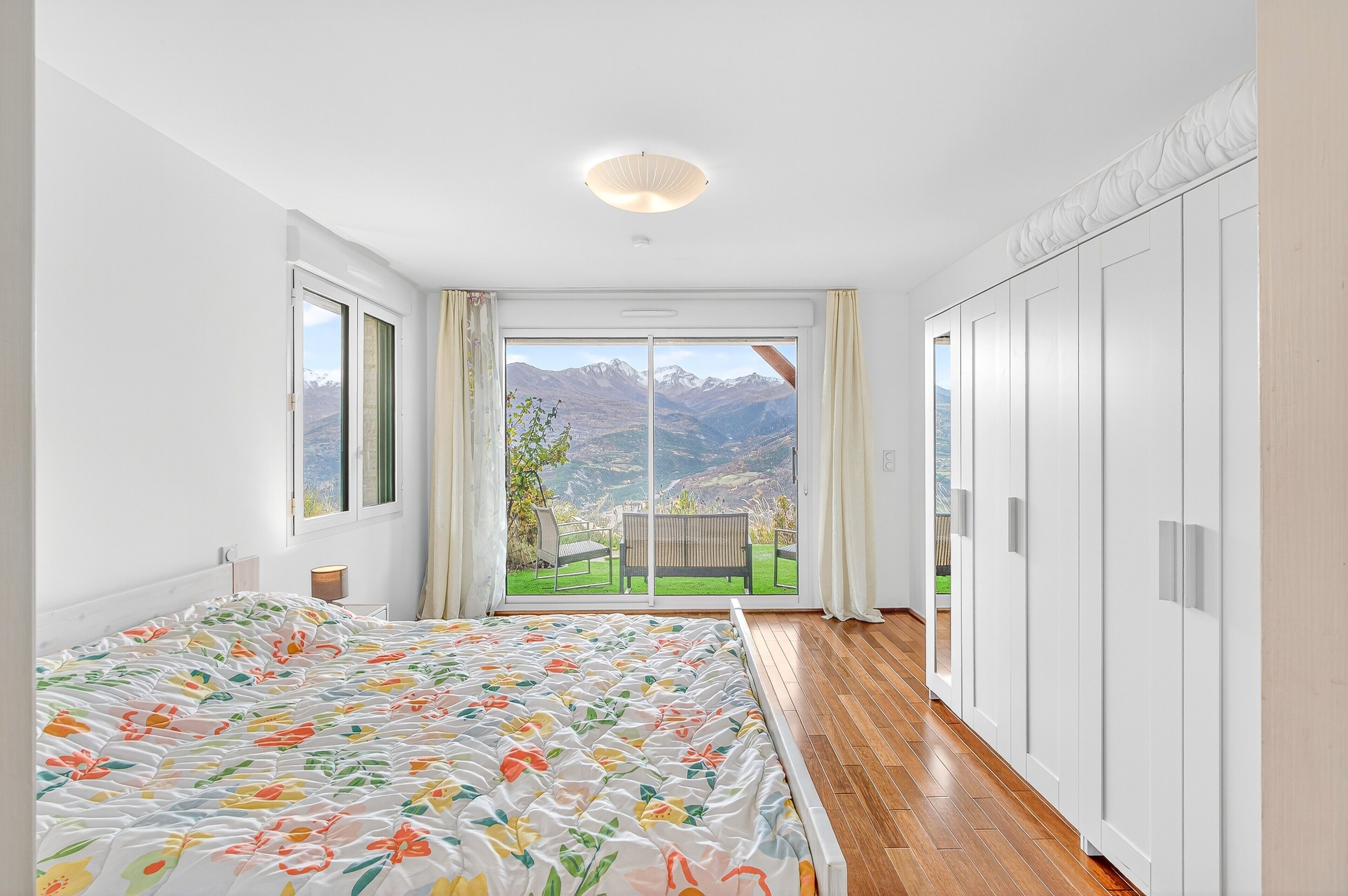 Una camera da letto con un letto grande, vista sulle montagne attraverso una porta scorrevole e pavimento in legno.