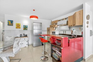 Une cuisine moderne avec une table à manger en verre, un tabouret de bar rouge, des meubles en bois et un réfrigérateur en acier inoxydable.