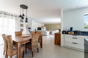 A modern kitchen with white cabinets, a wooden dining table with wicker chairs, and a hanging light fixture.