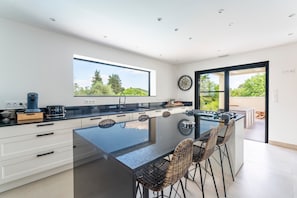 A modern kitchen with a large island, white cabinetry, and a view of greenery outside. - Villa 'Spacieuse Et Accueillante' with Pool, Terrace & Wi-Fi (St André d'olerargues)