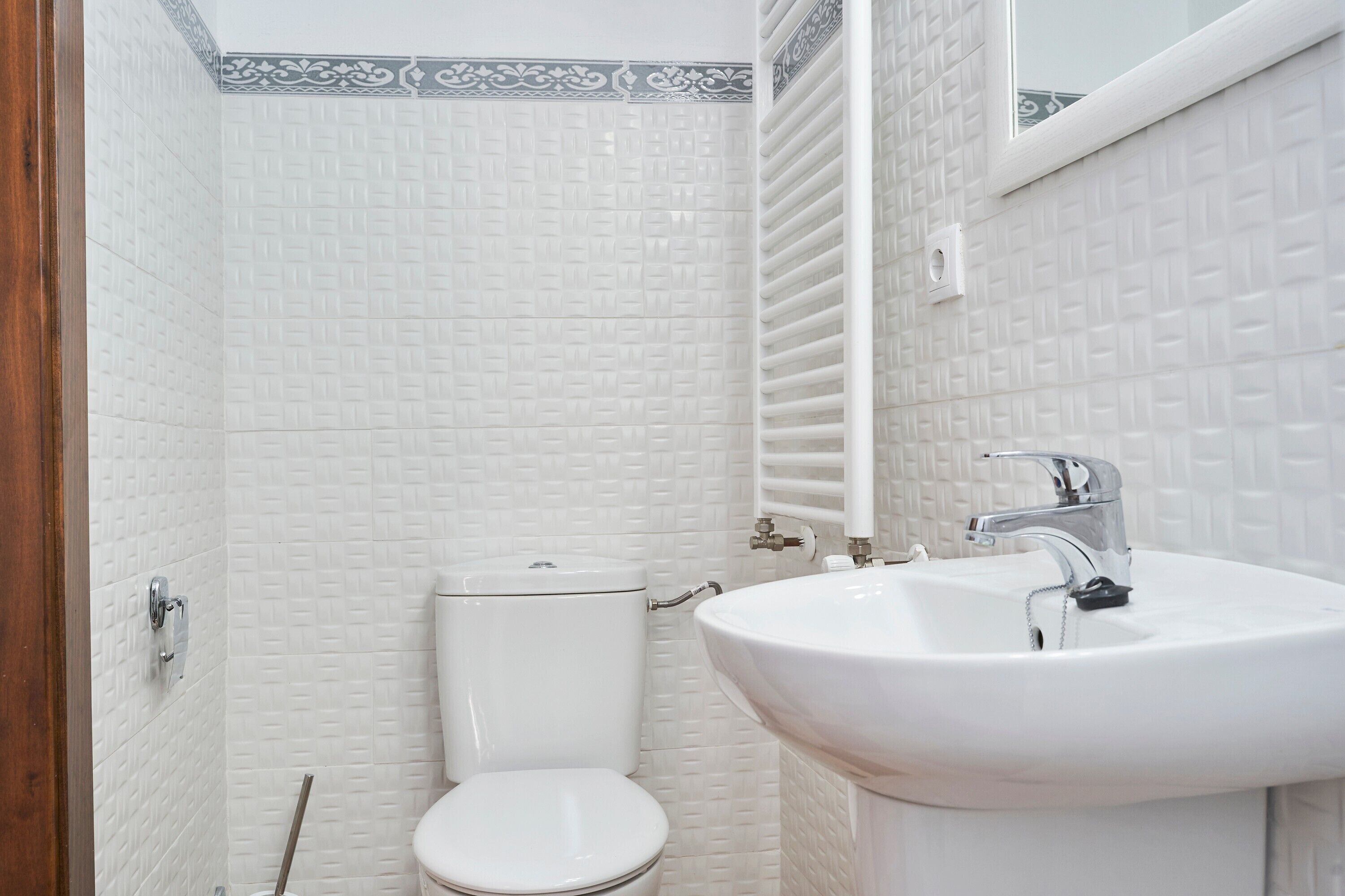 A bathroom with a white toilet, a sink with a mirror above it, and a wall with a decorative border.