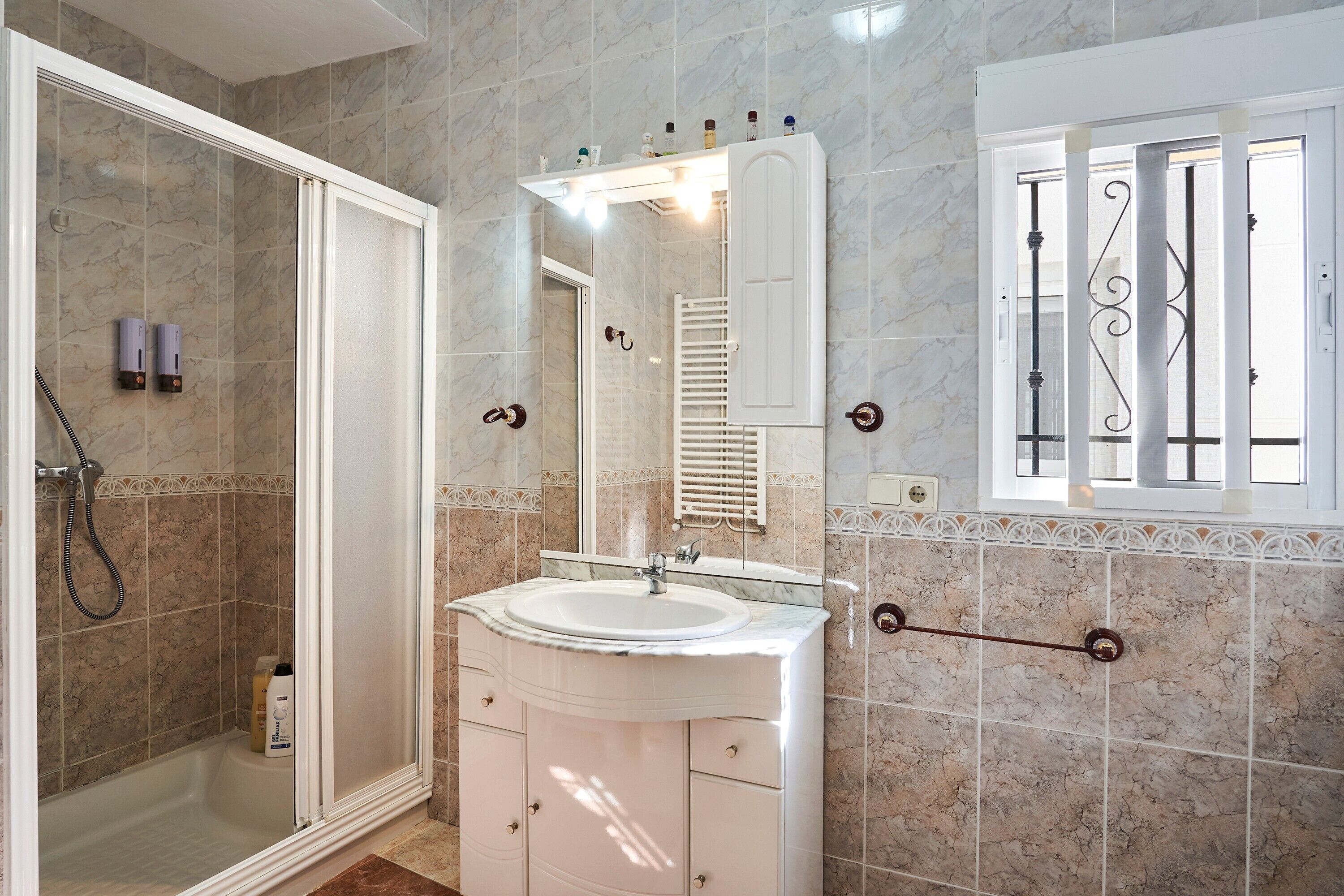 A bathroom with a shower, a sink, a mirror, and a window with bars.
