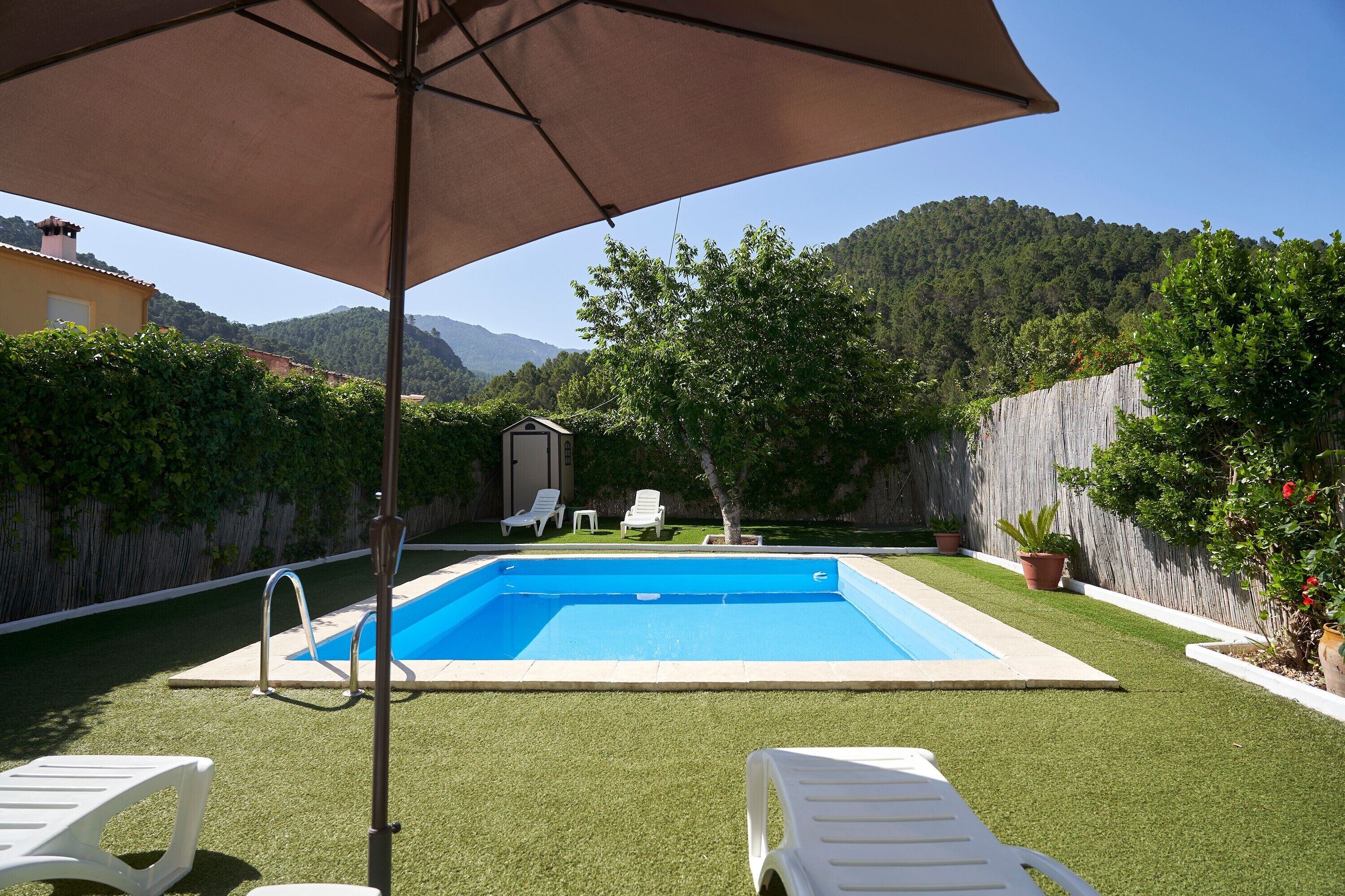 A swimming pool with artificial grass, white lounge chairs, and a wooden fence.