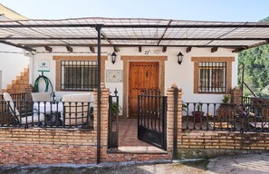 A house with a wooden door, a number '22' above it, a brick wall, a metal gate, and a covered porch area. - Holiday Home 'Alojamiento Rural Puente Honda' with Mountain View, Pool & Wi-Fi (Benatae)